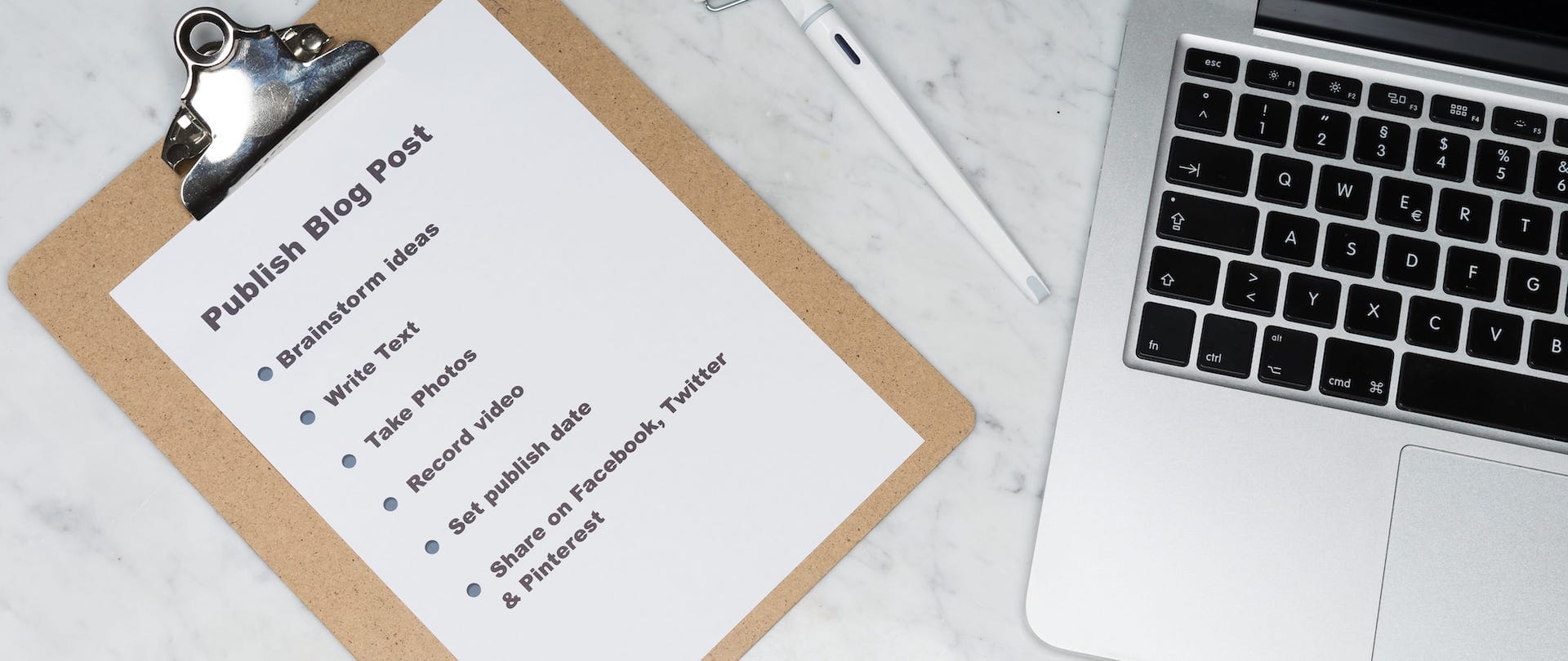A clipboard with a bullet list of tasks to publish a blog post next to a MacBook